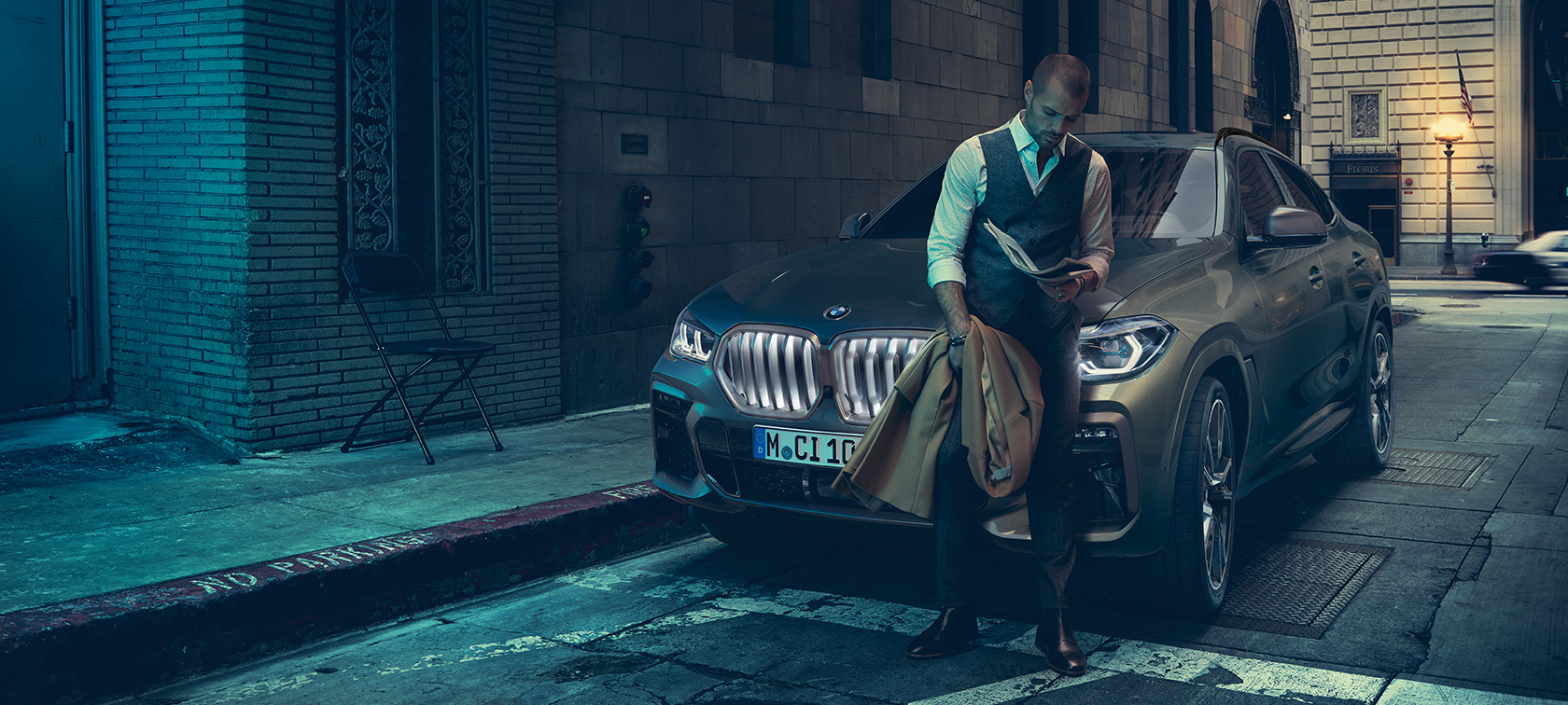 Man leunt tegen BMW X6 SUV G06. Man leunt tegen BMW X6 SUV in zijaanzicht in een stedelijke omgeving G06.