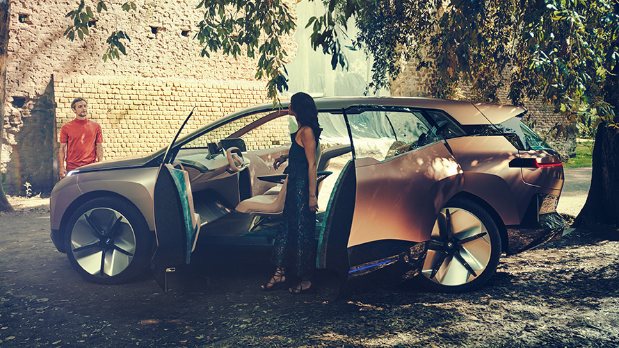 Zijaanzicht BMW Vision iNEXT Zijaanzicht BMW Vision iNEXT met vrouw bij open deur en man op de achtergrond