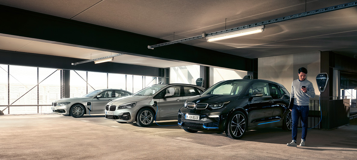 Voitures BMW électriques et hybrides devant une borne de recharge Avantages fiscaux BMW Voitures BMW électriques et hybrides, homme devant une borne de recharge