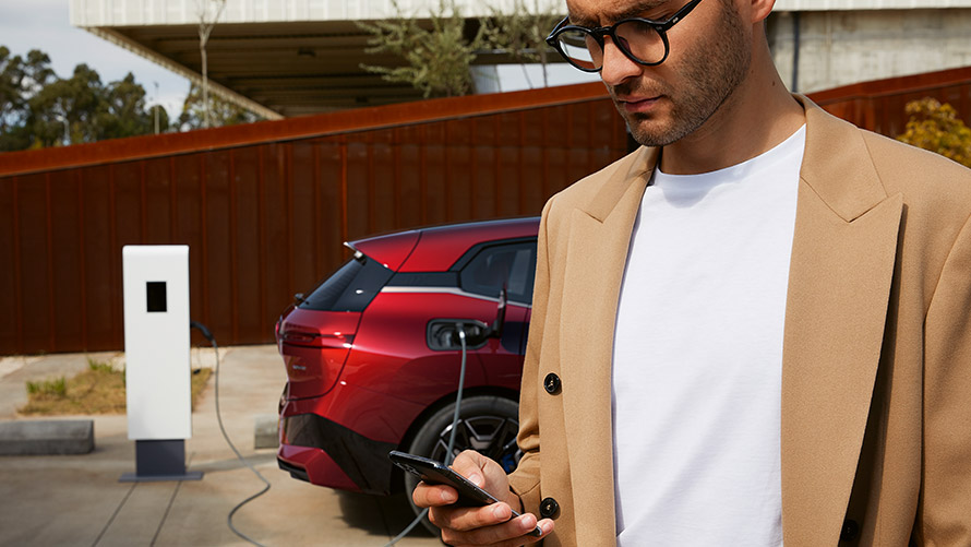 Vrouw met smartphone voor BMW iX3 aan laadstation Vrouw met smartphone voor BMW iX3 aan laadstation