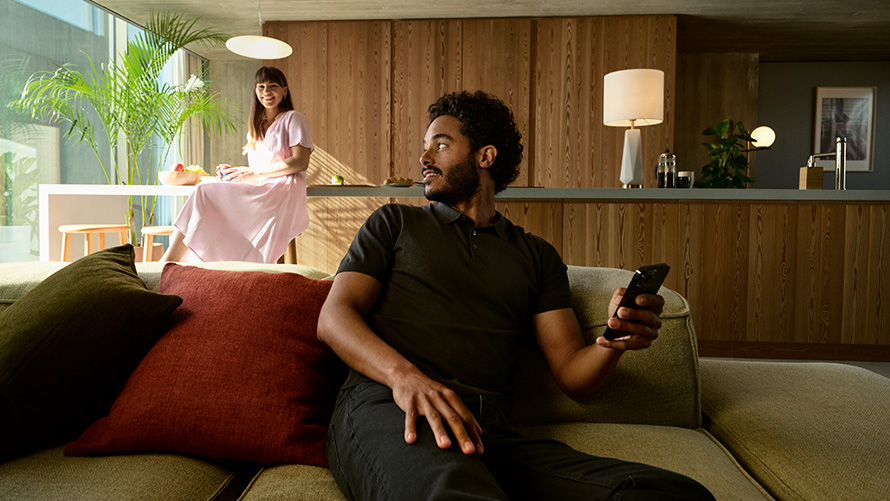 Delen BMW Digital Key BMW Digital Key delen man met smartphone in de hand zittend op de sofa met vrouw op de achtergrond