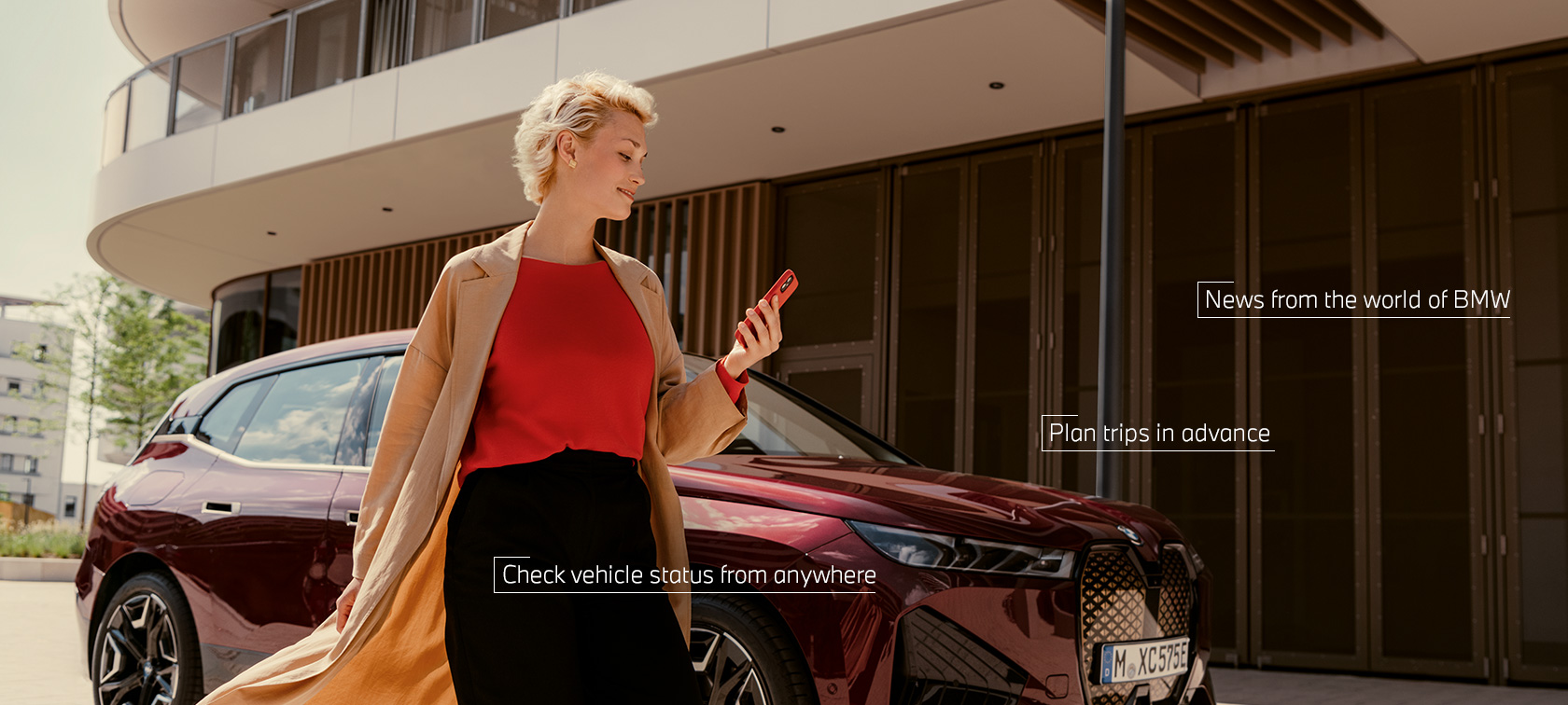 Vrouw staat voor witte BMW X5 en gebruikt My BMW App op smartphone Vrouw staat voor witte BMW X5 en gebruikt My BMW App op smartphone