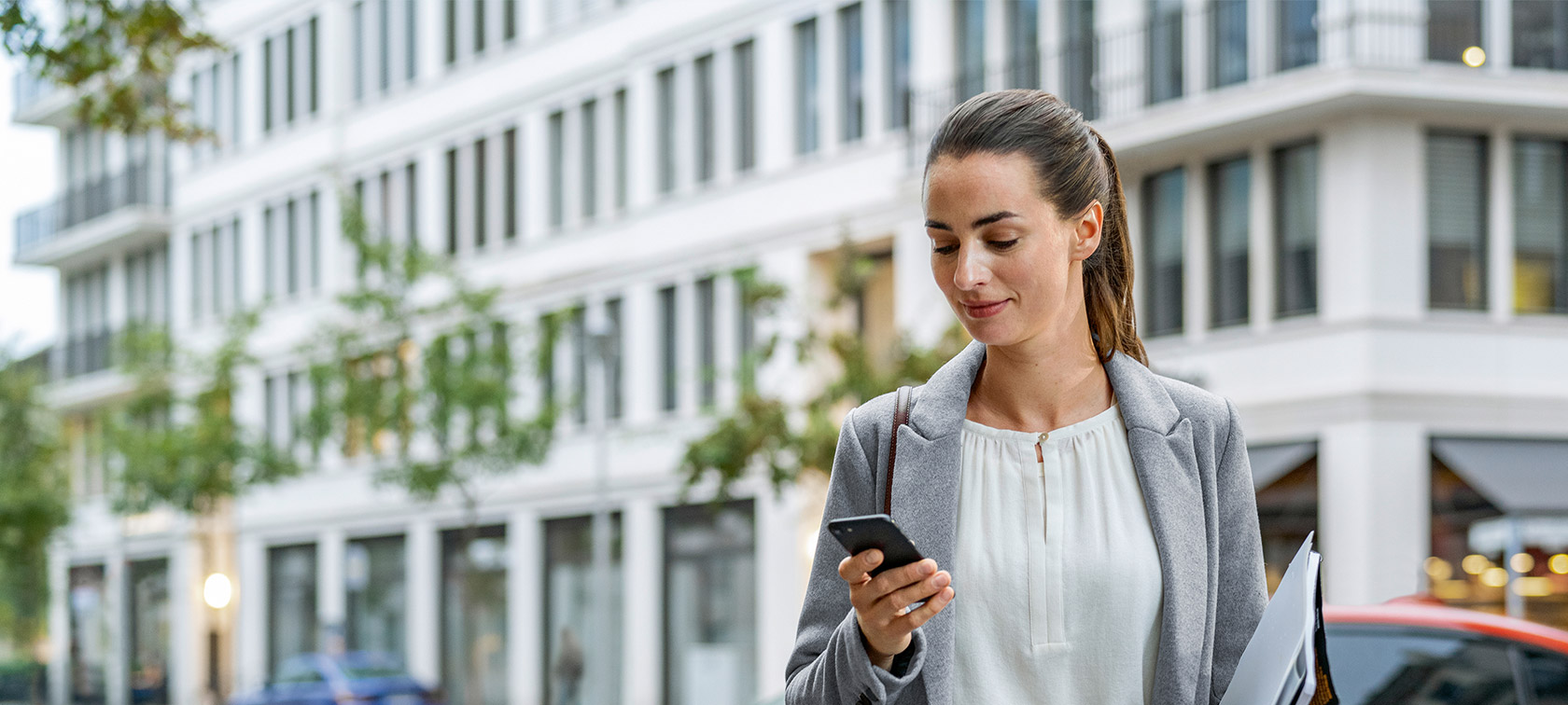 Femme debout devant un bâtiment et regardant son smartphone Remote Software Upgrade Femme debout devant un bâtiment et regardant son smartphone