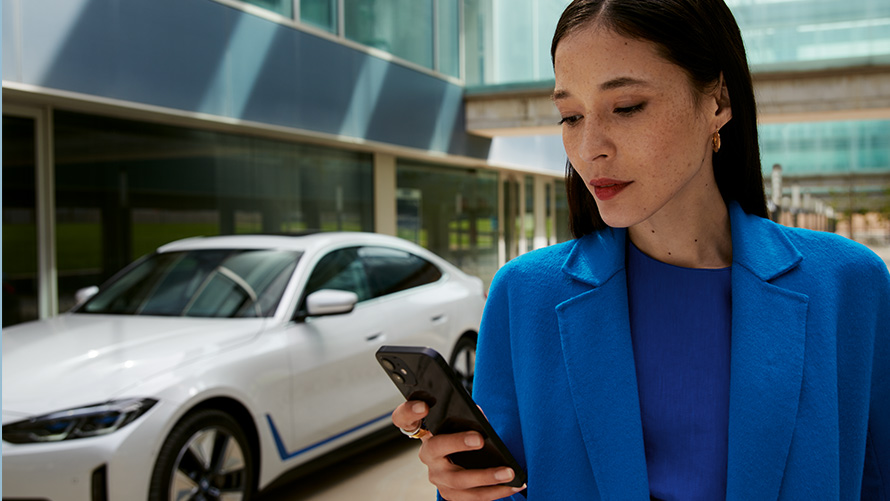 Vrouw staand voor een BMW Vrouw staat voor een BMW en kijkt op haar smartphone