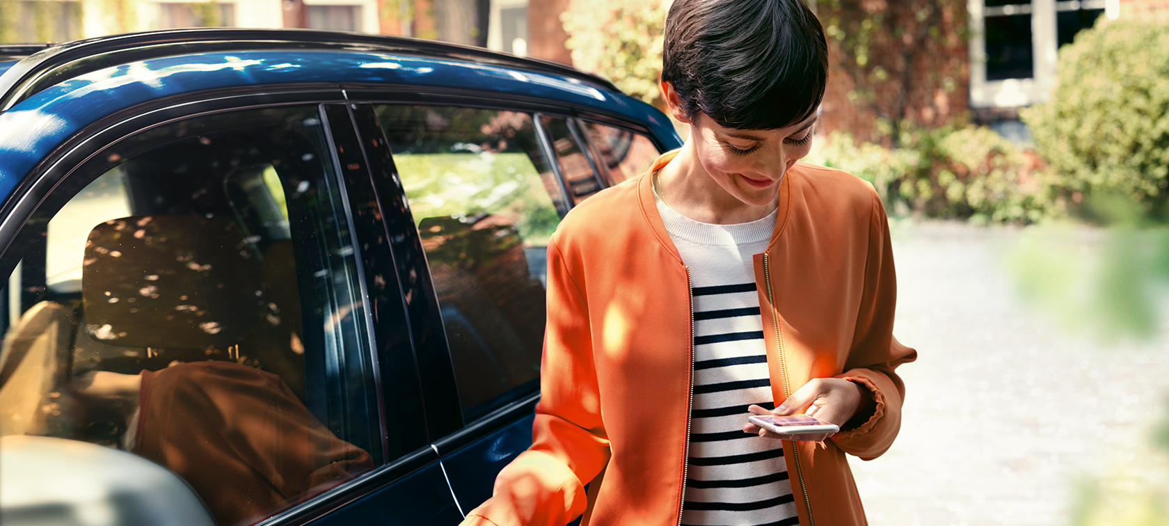 Donkerharige vrouw voor BMW Donkerharige vrouw in oranje jasje voor BMW kijkt op haar smartphone