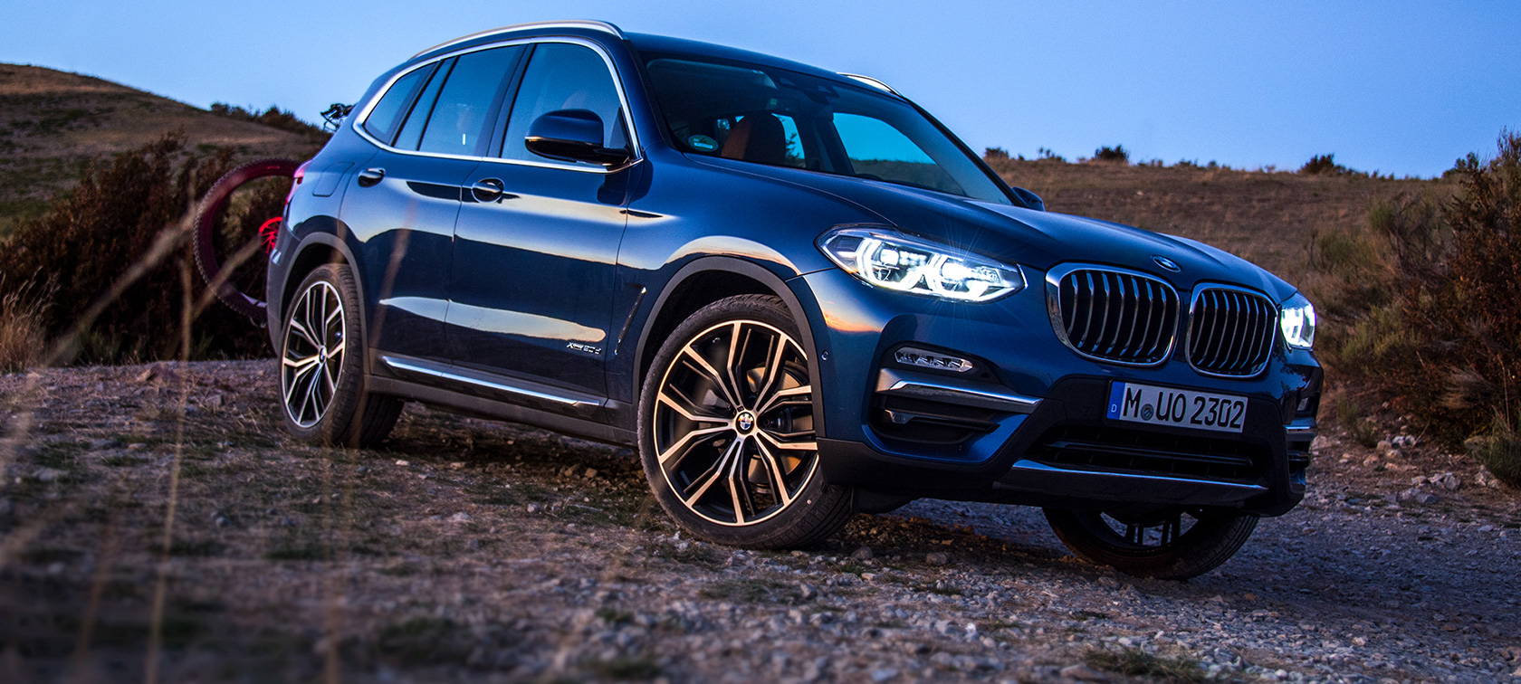 Donkerblauwe BMW X3 op ruw terrein Donkerblauwe BMW X3 stilstaand met achterdrager en mountainbike op ruw terrein