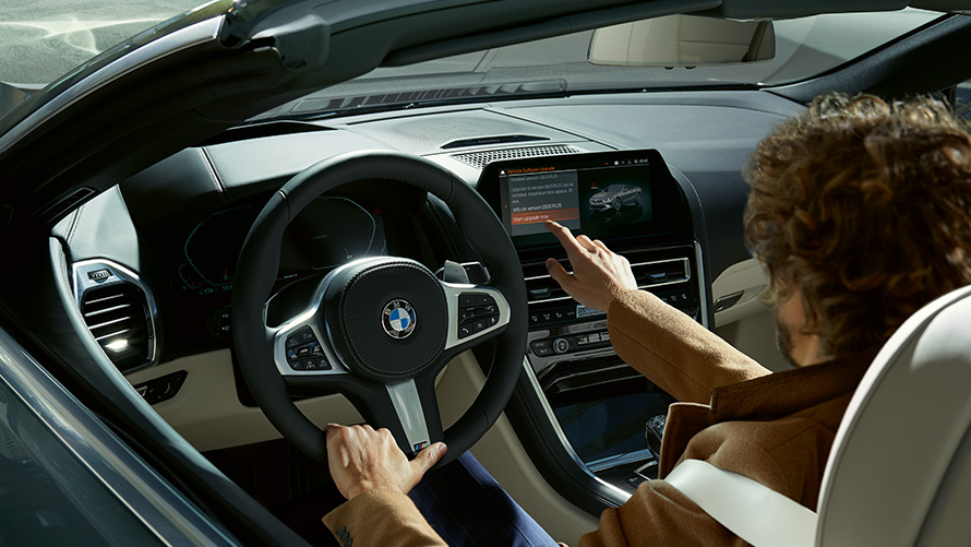 Remote Software Upgrade Remote Software Upgrade, un homme est assis dans la BMW et commande le Control Display