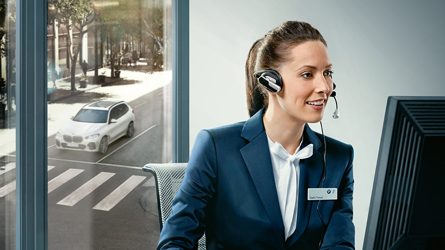Concierge Service Concierge Services : une collaboratrice de BMW portant un casque d'écoute est assise devant un écran.