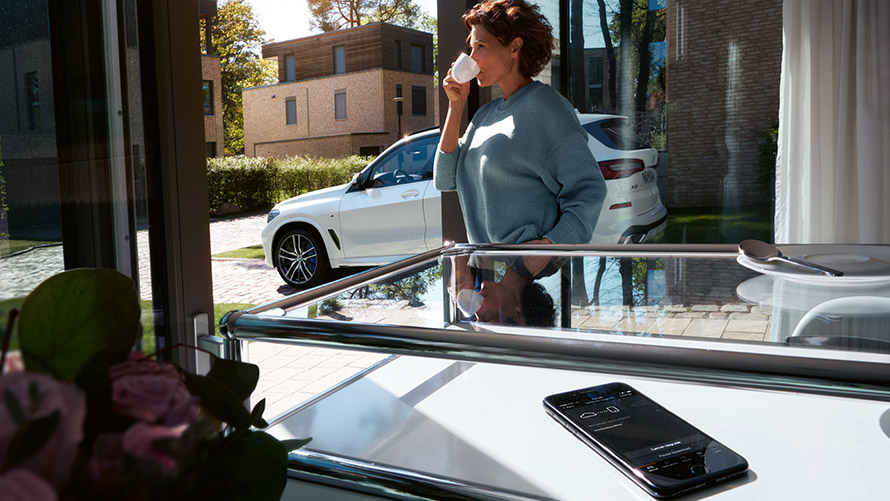 Remote Software Upgrade Une femme savoure un café chez elle tandis qu'a lieu la mise à jour Remote Software Upgrade sur son smartphone.