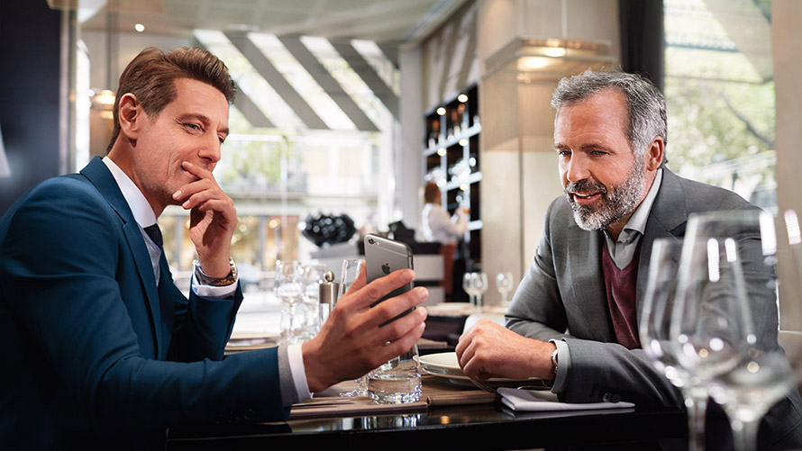 Gérez vos destinations favorites Deux hommes au restaurant utilisent la fonction "Gérez vos destinations favorites" sur un smartphone.
