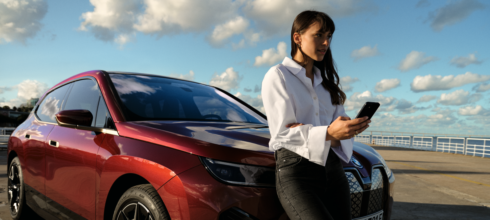 Vrouw staat voor witte BMW X5 en gebruikt My BMW App op smartphone Vrouw staat voor witte BMW X5 en gebruikt My BMW App op smartphone