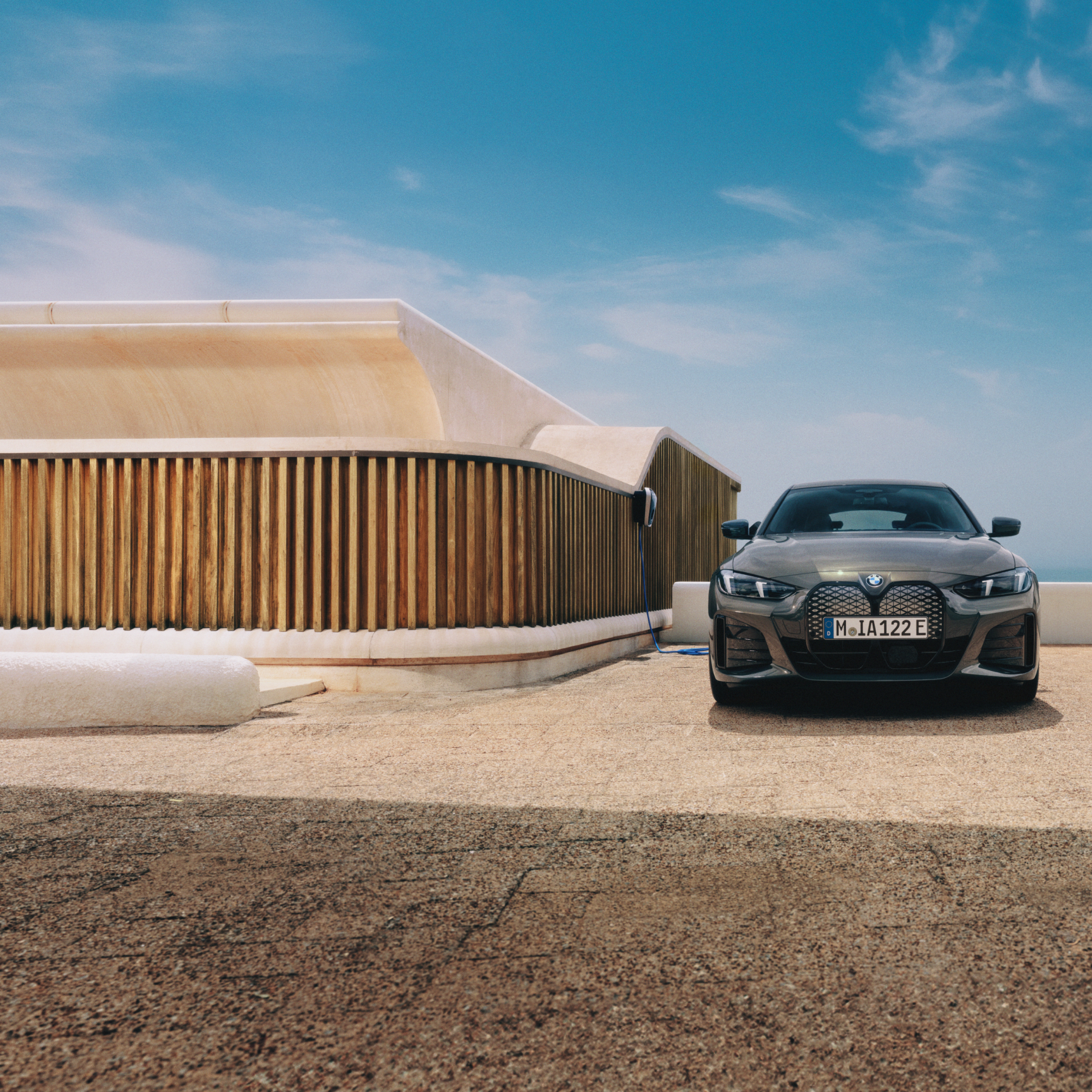 Een man met een smartphone staat naast een BMW i4 die is aangesloten op een wallbox